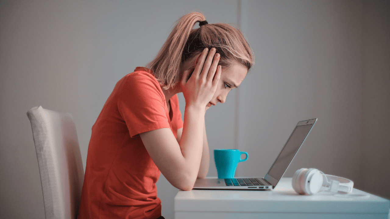 Frustrated woman with hand placed on her head while looking at a laptop