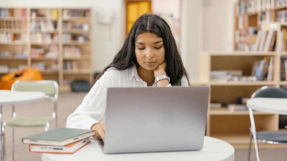 Woman studying with laptop and books at a library.