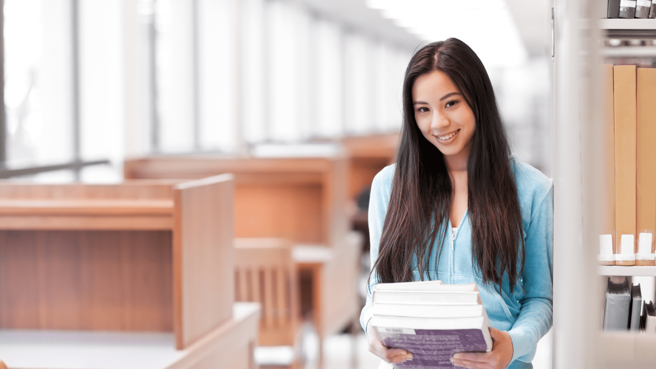 A medical school student in a library holding several Step 2 CK review books.